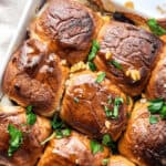 A dish of baked steak and cheese sliders garnished with chopped herbs in a white casserole.