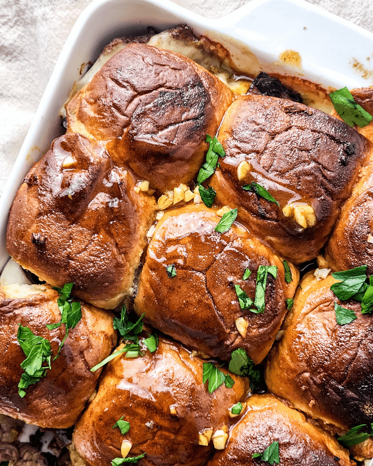 A dish of baked steak and cheese sliders garnished with chopped herbs in a white casserole.