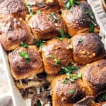 Baked steak and cheese sliders garnished with fresh parsley in a white baking dish.