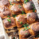 Baked steak and cheese sliders garnished with fresh parsley in a white baking dish.