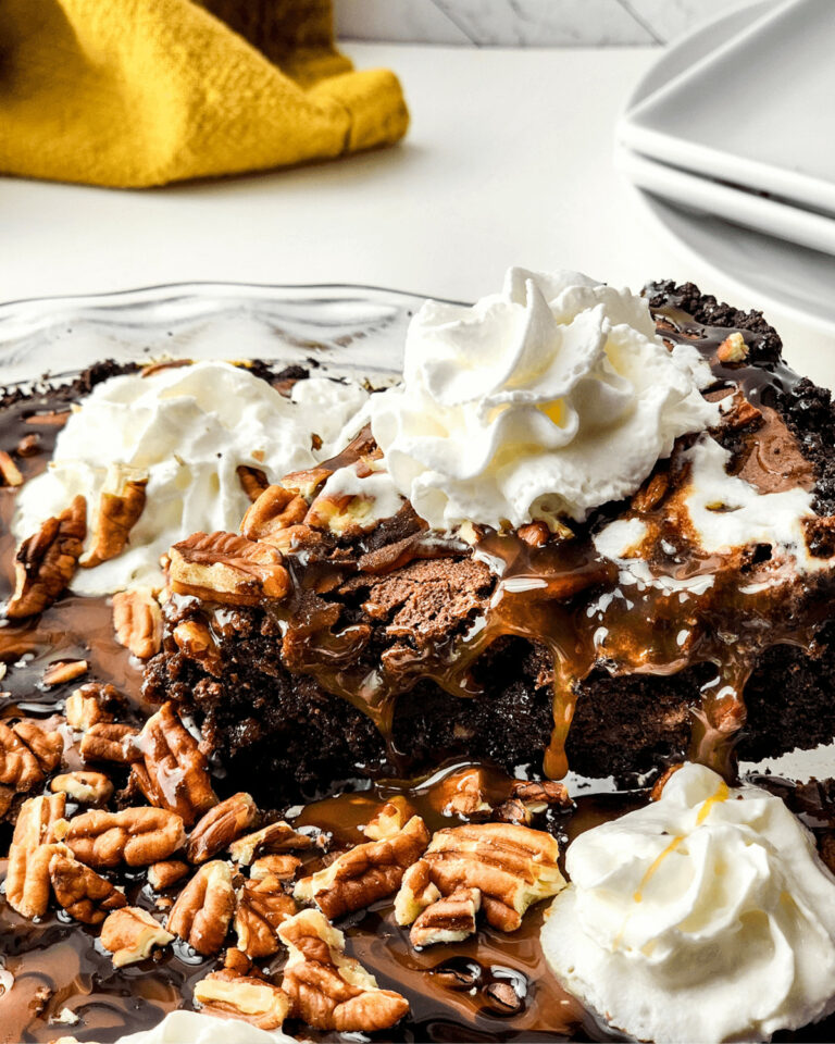 Slice of chocolate brownie pie topped with whipped cream on a plate with chocolate syrup drizzle.