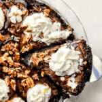 A slice of brownie pie with whipped cream and pecans on top.