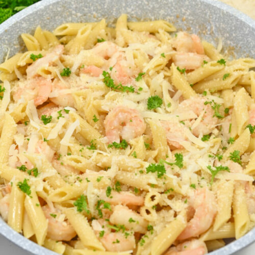 A bowl of shrimp pasta garnished with parsley and grated cheese, served with a slice of bread.