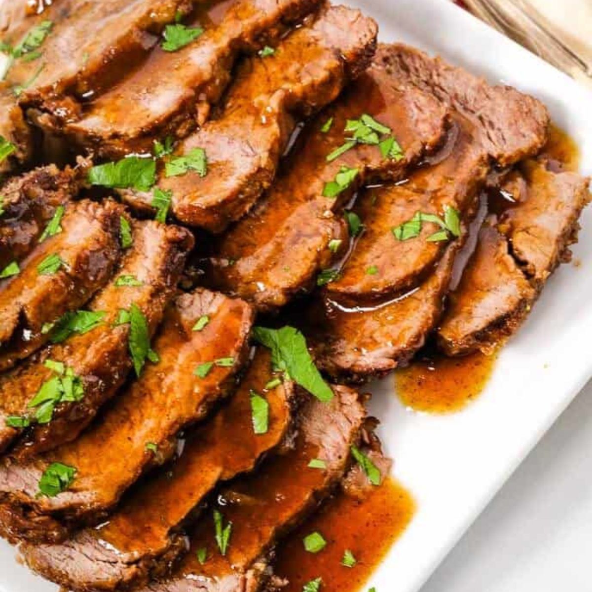 Sliced roast beef topped with gravy, garnished with chopped parsley on a white plate, featured in our recipe index.