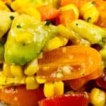 Close-up of a salad with corn, avocado, cherry tomatoes, and diced red pepper, mixed in a light dressing—perfect as a fresh side for baked haddock.