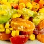 Close-up of a salad with cherry tomatoes, corn, avocado, and carrots.