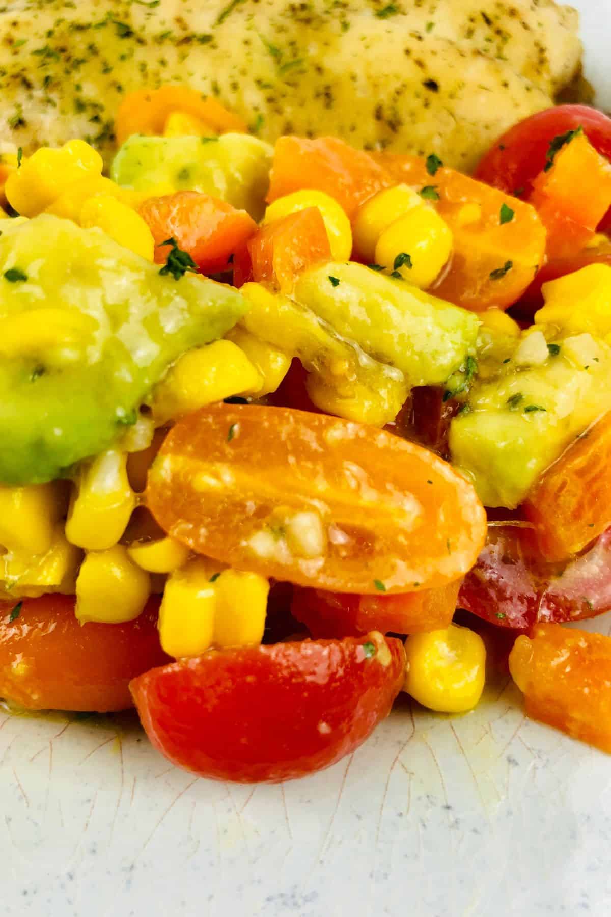 Close-up of a salad with cherry tomatoes, corn, avocado, and carrots.