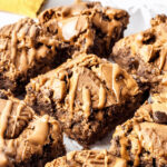 Close-up of chunky biscoff brownies on a white plate, drizzled with melted peanut butter.