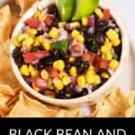 A bowl of Black Bean and Corn Salsa garnished with lime wedges, surrounded by crispy tortilla chips.