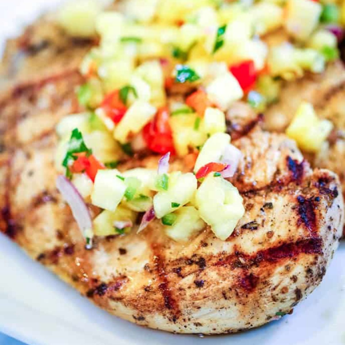 Grilled chicken breast topped with a colorful diced pineapple salsa, served on a white plate and featured in our recipe index.
