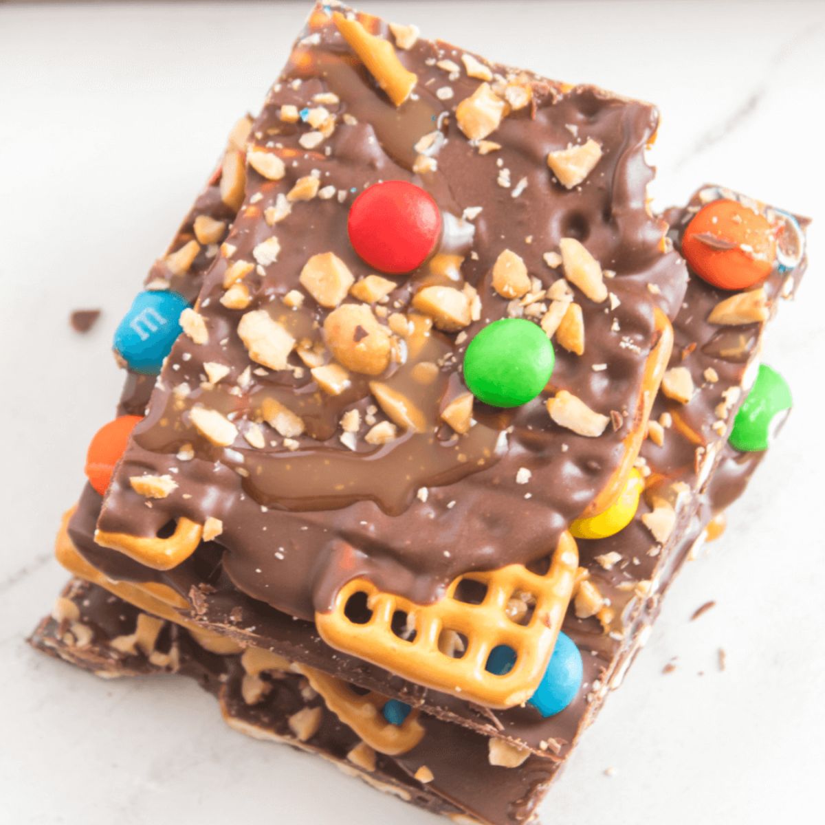 A recipe index featuring a stack of chocolate bark topped with pretzels, nuts, and colorful candy pieces on a white surface.