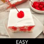 Slice of cherry poke cake topped with whipped cream and a cherry on a white plate, with a bowl of cherries and part of the cherry poke cake in the background.