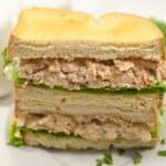 A plate with a sandwich cut in half, , stacked with toasted bread slices.