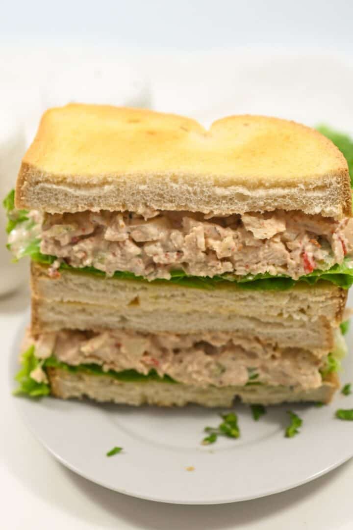 A plate with a sandwich cut in half, , stacked with toasted bread slices.