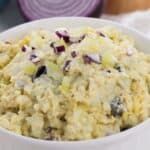 A white bowl filled with Classic Egg Salad, topped with chopped celery and red onion pieces, with a sliced red onion in the background.