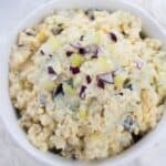A bowl of Classic Egg Salad topped with chopped red onions, served on a white surface.