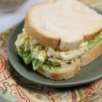 A sandwich with lettuce on white bread, served on a green plate and placed on a patterned cloth.