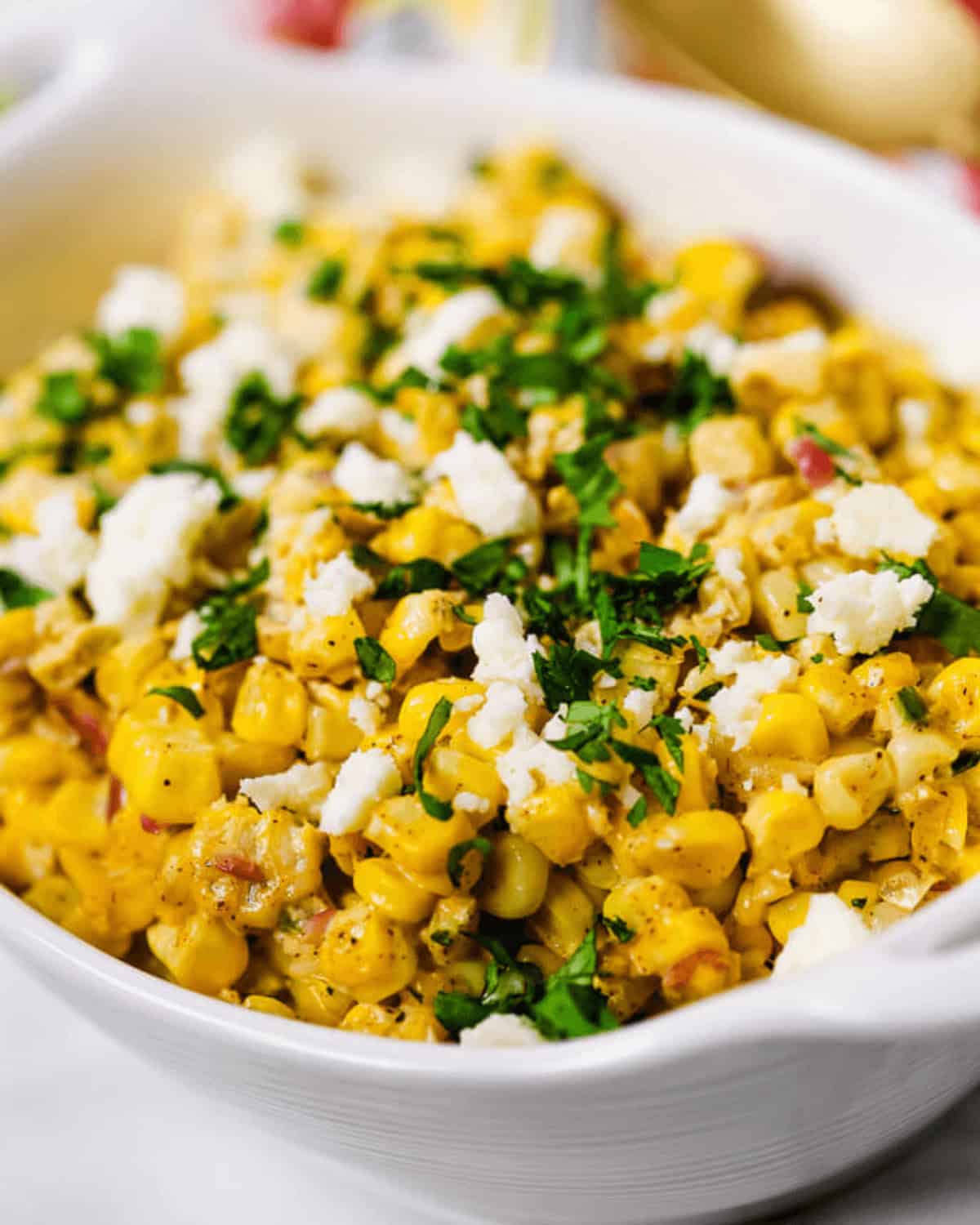 A white bowl filled with flavorful Elote Salad—seasoned corn topped with crumbled cheese and chopped fresh herbs.