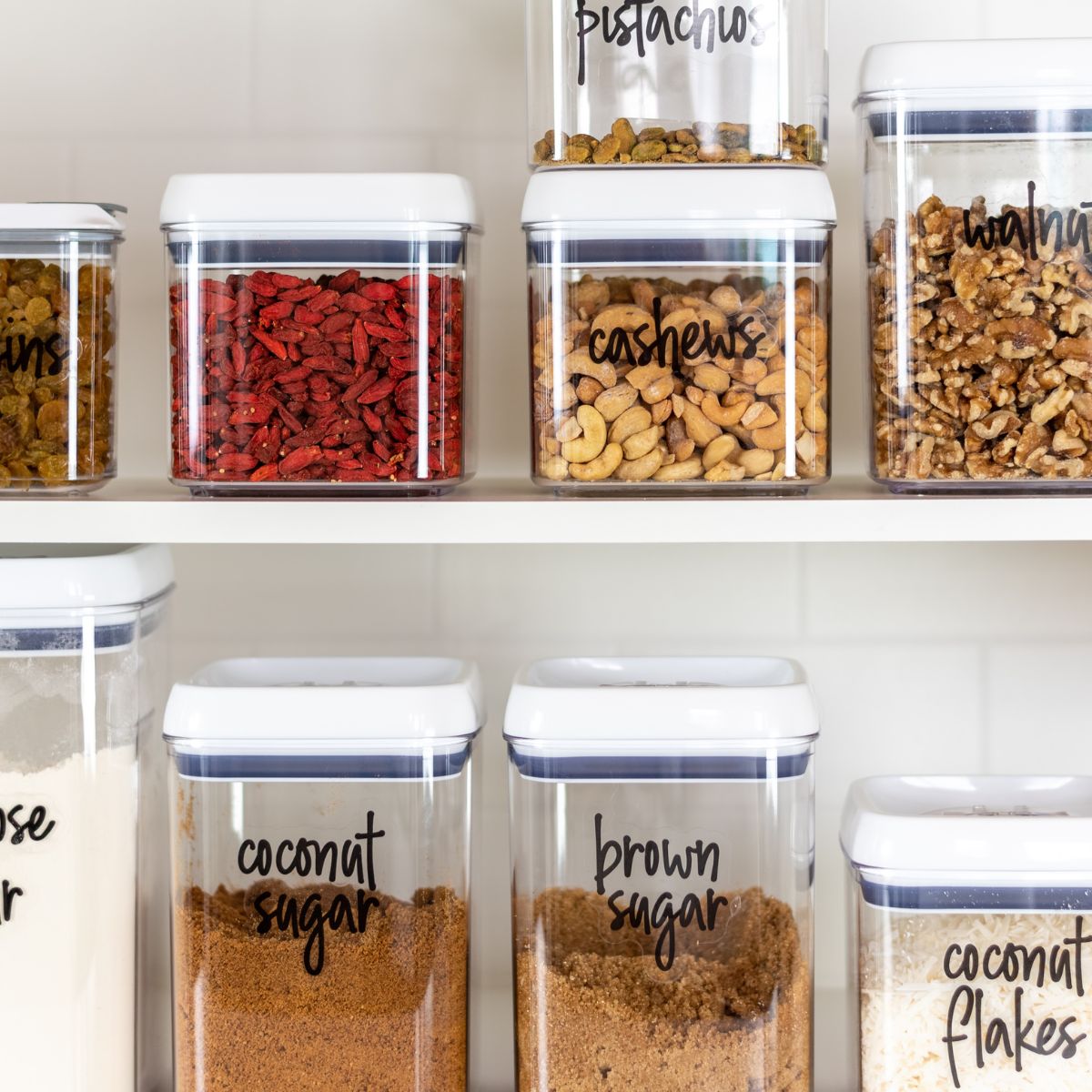 Clear containers with various ingredients labeled on white shelves, including nuts and sugars, organized by a recipe index.