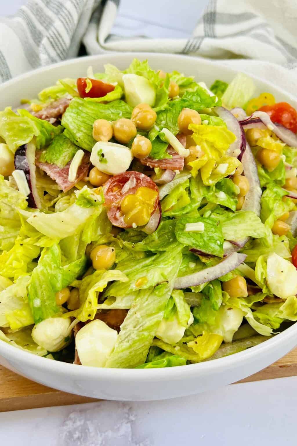 A bowl of Italian Chopped Salad with lettuce, cherry tomatoes, chickpeas, mozzarella balls, red onion, and a light dressing.