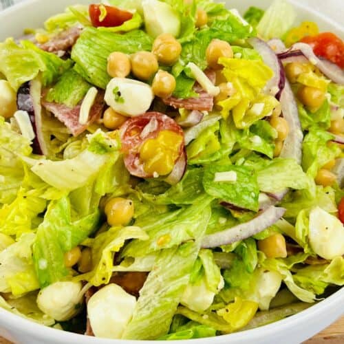 A bowl of Italian Chopped Salad with lettuce, cherry tomatoes, chickpeas, mozzarella balls, red onion, and a light dressing.