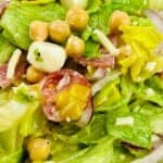 Close-up of a fresh Italian Chopped Salad featuring crisp lettuce, cherry tomatoes, chickpeas, red onion, mozzarella balls, shredded cheese, and savory slices of salami.