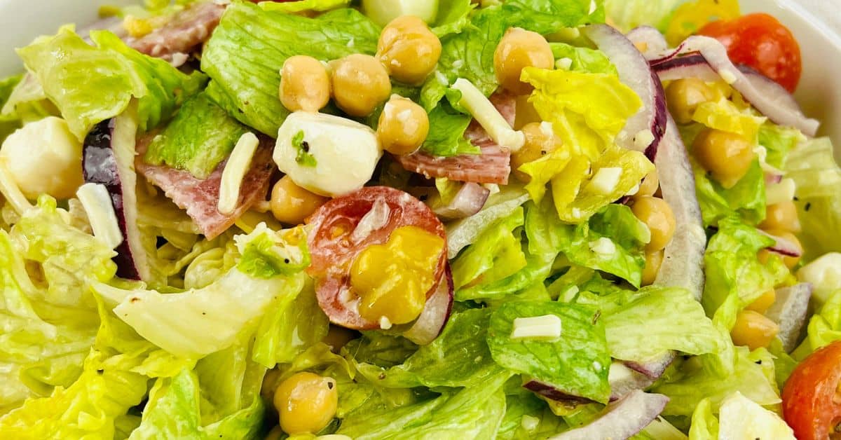 Close-up of a fresh Italian Chopped Salad featuring crisp lettuce, cherry tomatoes, chickpeas, red onion, mozzarella balls, shredded cheese, and savory slices of salami.