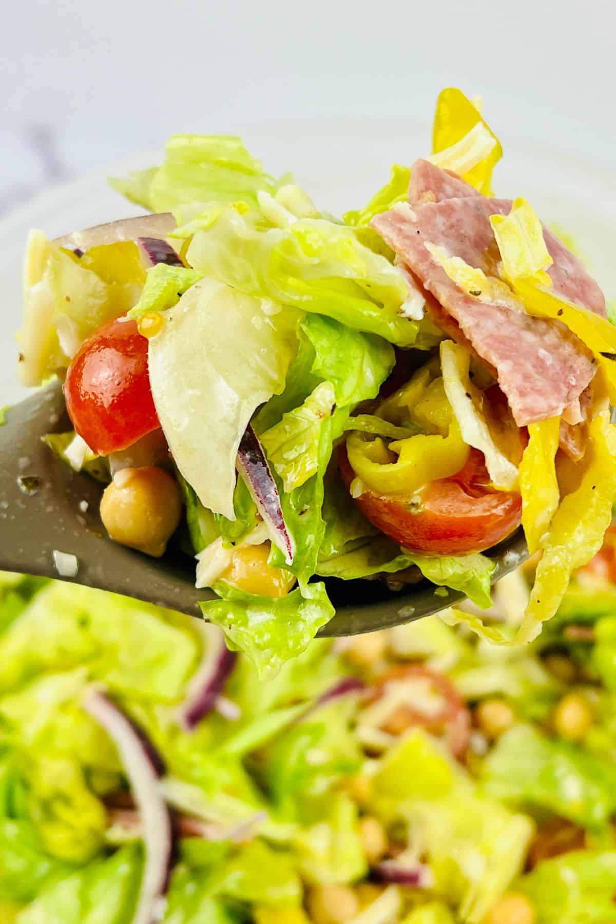 Close-up of a spoonful of Italian Chopped Salad with lettuce, cherry tomatoes, red onion, chickpeas, sliced salami, shredded cheese, and pepperoncini.