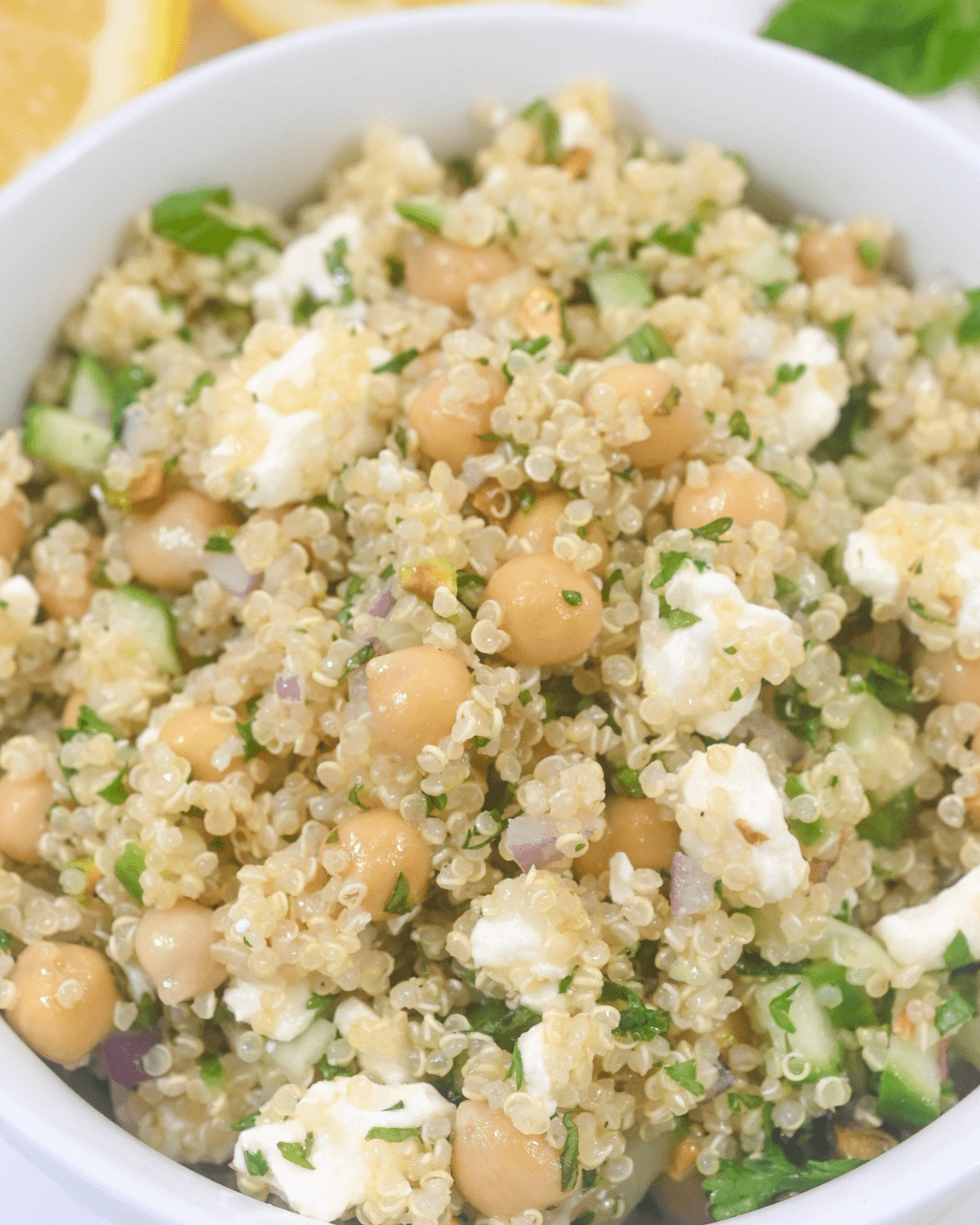 A bowl of Jennifer Aniston salad with quinoa, chickpeas, cucumber, feta cheese, and herbs, garnished with lemon slices.