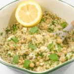 A bowl of Jennifer Aniston salad with chickpeas, parsley, and a lemon slice on top, served in a green and white bowl.