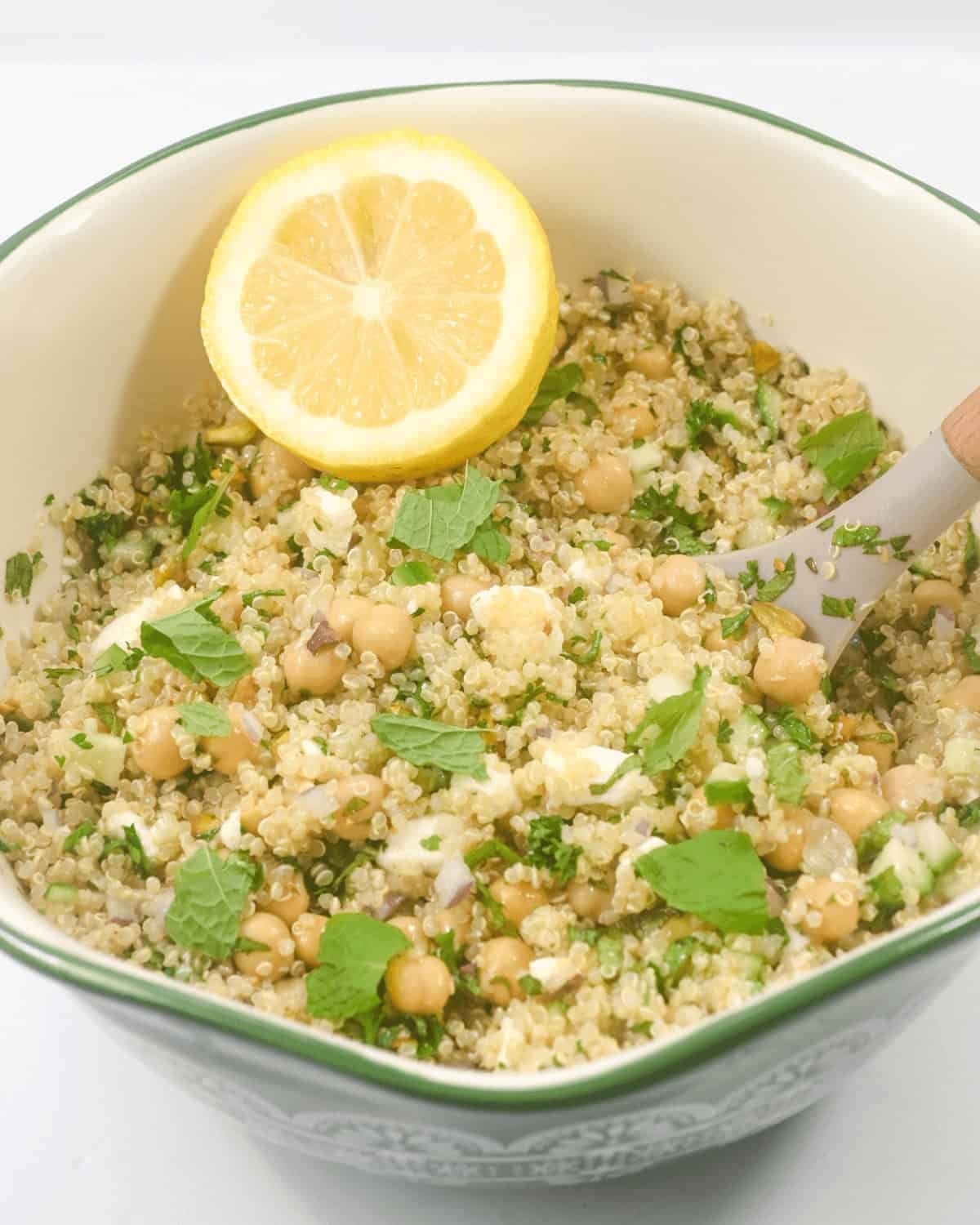 A bowl  with chickpeas, parsley, and a lemon slice on top, served in a green and white bowl.