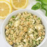 A bowl of Jennifer Aniston salad with chickpeas, feta cheese, cucumber, and fresh herbs, garnished with lemon slices.
