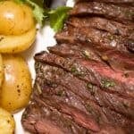 Marinated Skirt Steak, sliced medium-rare and garnished with herbs, served with roasted baby potatoes and mixed greens on a white plate.