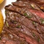Marinated Skirt Steak, sliced and grilled with visible herbs, served alongside seasoned roasted potatoes on a white plate.