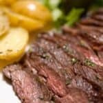 Sliced medium-rare meat and garnished with herbs, served with roasted baby potatoes and a side of mixed greens.