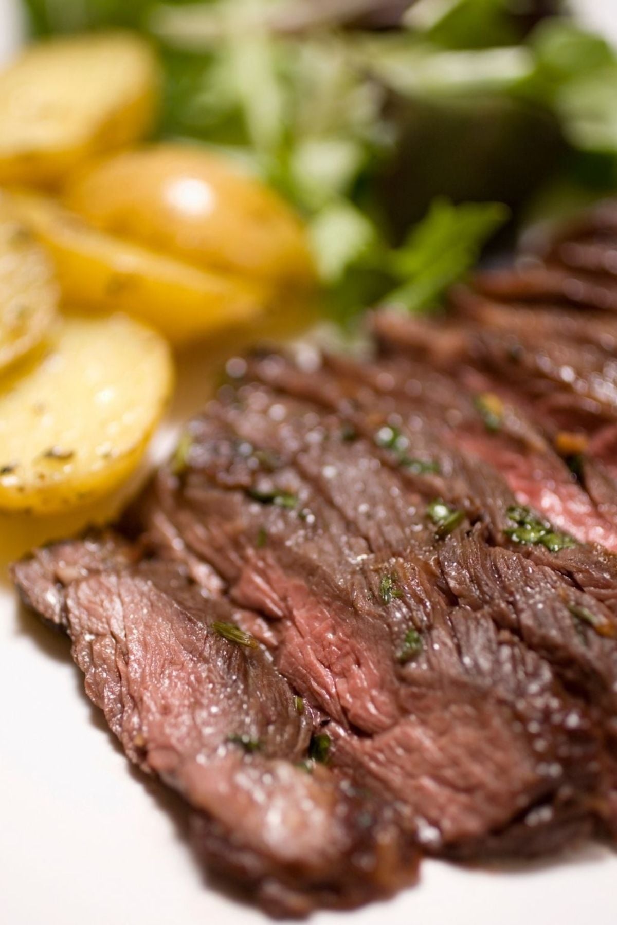  Sliced medium-rare meat and garnished with herbs, served with roasted baby potatoes and a side of mixed greens.