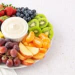 A plate with strawberries, blackberries, blueberries, kiwi slices, pineapple, grapes, mandarin orange segments, apple slices, and a bowl of Marshmallow Fluff Fruit Dip in the center.