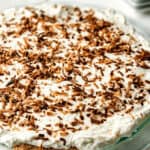 An old-fashioned homemade coconut cream pie topped with whipped cream and sprinkled with chocolate shavings, served on a glass plate.