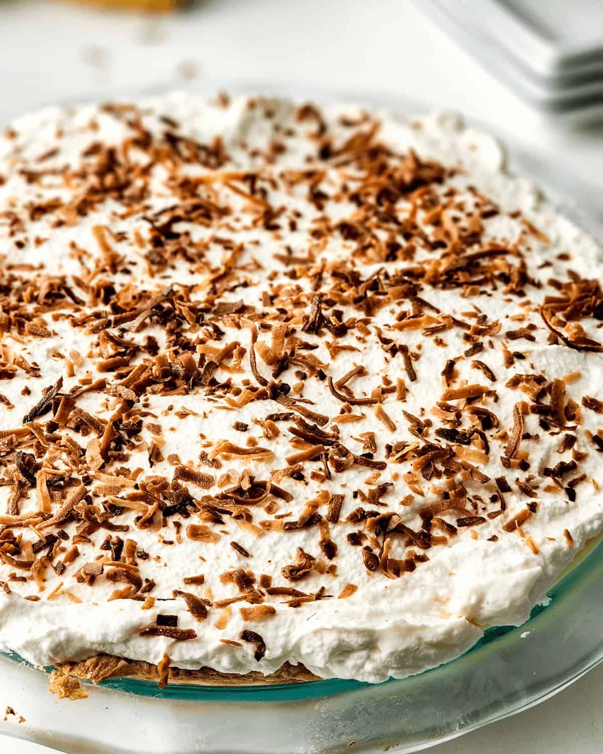 An old-fashioned homemade coconut cream pie topped with whipped cream and sprinkled with chocolate shavings, served on a glass plate.