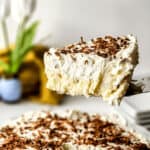 A slice of creamy old-fashioned coconut cream pie topped with chocolate shavings, with the remainder of the pie in the background.