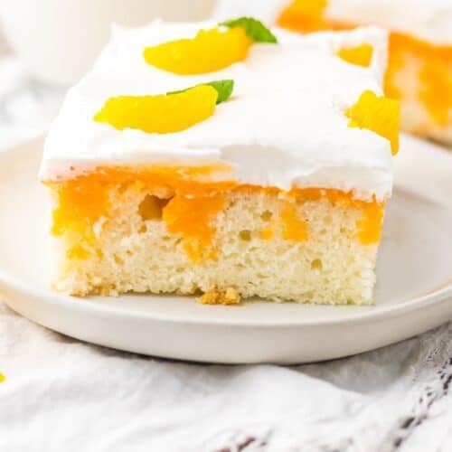 A slice of Orange Creamsicle Cake topped with whipped cream, orange segments, and a small mint leaf, served on a white plate.