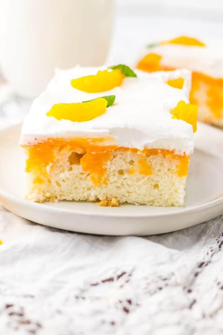 A slice of Orange Creamsicle Cake topped with whipped cream, orange segments, and a small mint leaf, served on a white plate.