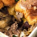 A close-up of a baked casserole with golden brown biscuits, melted cheese, sliced beef reminiscent of steak and cheese sliders, and caramelized onions in a white dish.