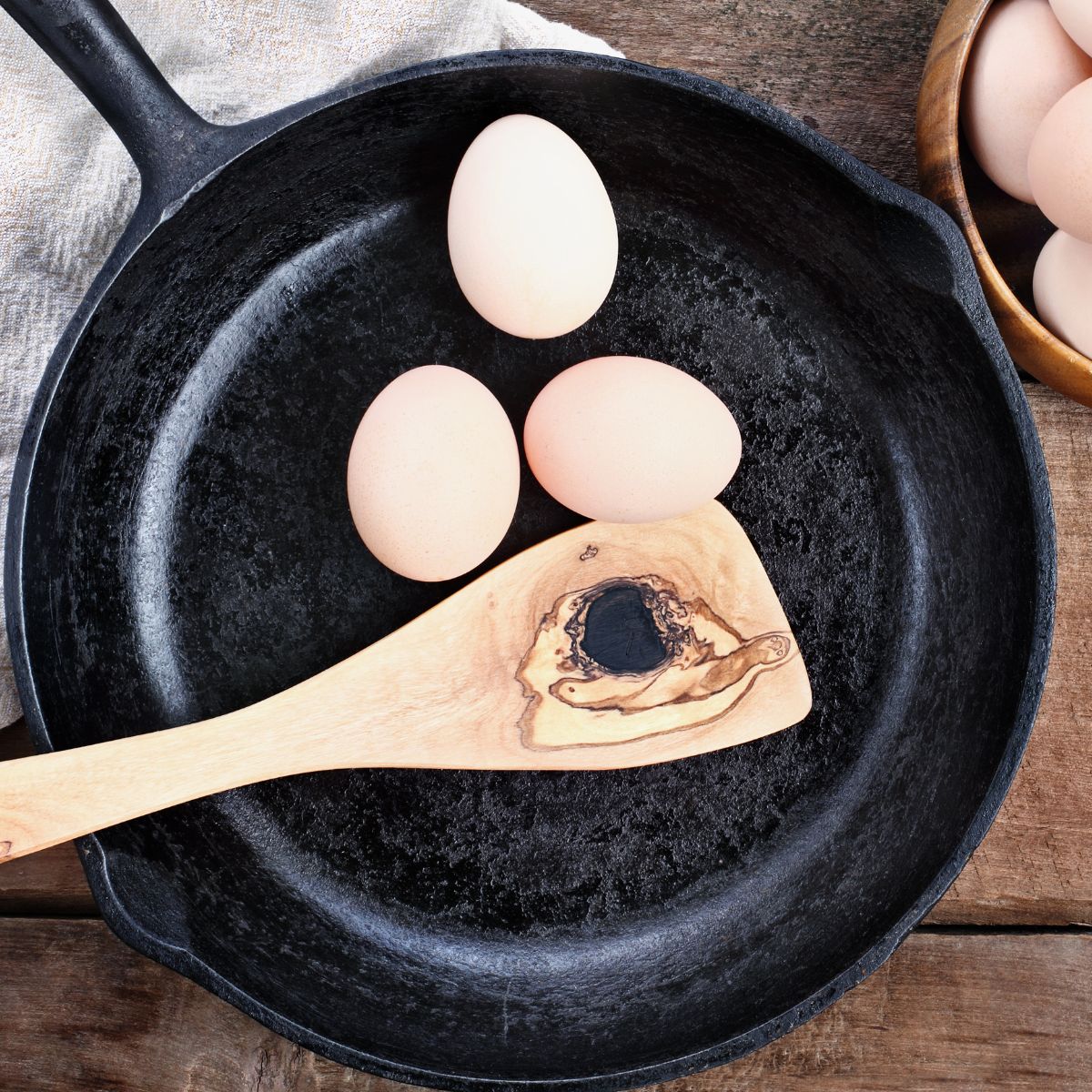 Three whole eggs and a wooden spoon in a cast iron skillet, set on a recipe index.