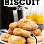 Plate of sugar-coated Air Fryer Biscuit Donuts in front of an air fryer, with text reading "Air Fryer Biscuit Donuts Easy." A glass of orange juice is visible in the background.