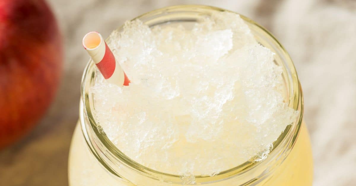 A close-up of a glass filled with crushed ice and a red-and-white striped paper straw, perfect for serving an Apple Cider Slush.
