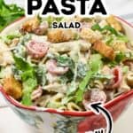 A bowl of creamy Caesar Pasta Salad with penne, lettuce, cherry tomatoes, and croutons, all tossed in Caesar dressing. Text on image reads: "Caesar Pasta Salad Creamy.