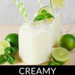 Two creamy coconut mojitos in mason jars with lime slices and mint, served with green-striped straws, beside fresh limes and mint leaves.