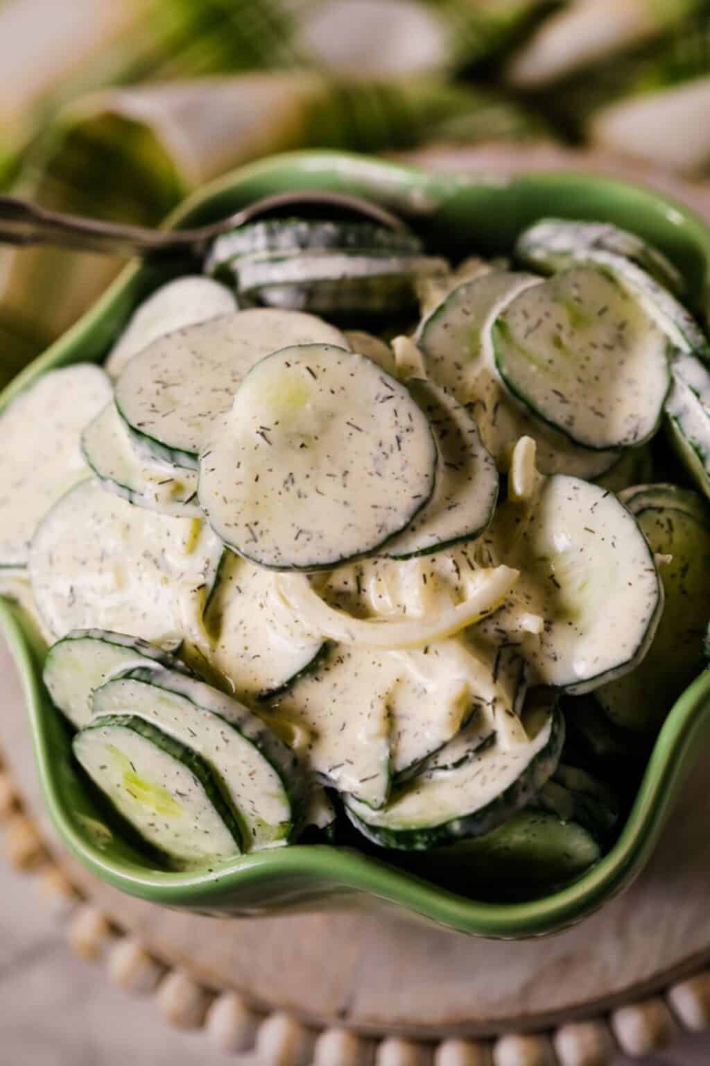 A green bowl filled with Cucumber Onion Salad—sliced cucumbers and onions coated in a creamy dill dressing.
