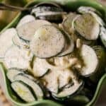 A green bowl filled with Cucumber Onion Salad—sliced cucumbers and onions coated in a creamy dill dressing.
